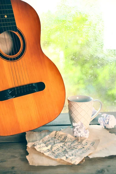 Chitarra acustica e tazza di tè accanto alla finestra con gocce di pioggia — Foto Stock