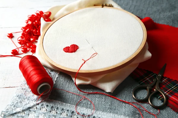 El aro de bordado con tela e hilos de coser rojos en la mesa de cerca — Foto de Stock