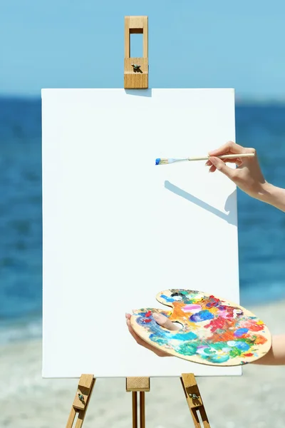 Палитра для женских рук с красками и мольбертом на пляже — стоковое фото