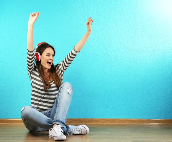 Young woman sitting on floor with headphones on turquoise wallpaper background — Stock Photo, Image