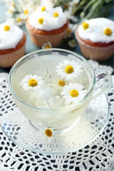 Cup of chamomile tea with chamomile flowers and tasty muffins on color wooden background — Stock Photo, Image