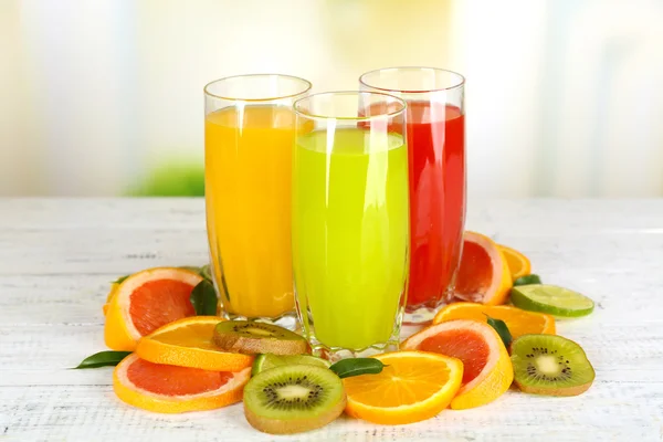 Vasos de diferentes jugos con frutas y menta sobre fondo brillante —  Fotos de Stock