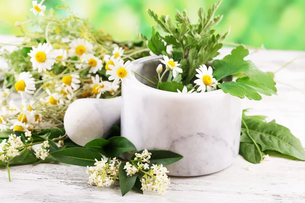 Herbs and flowers with mortar, on wooden table, on bright background — Stock Photo, Image