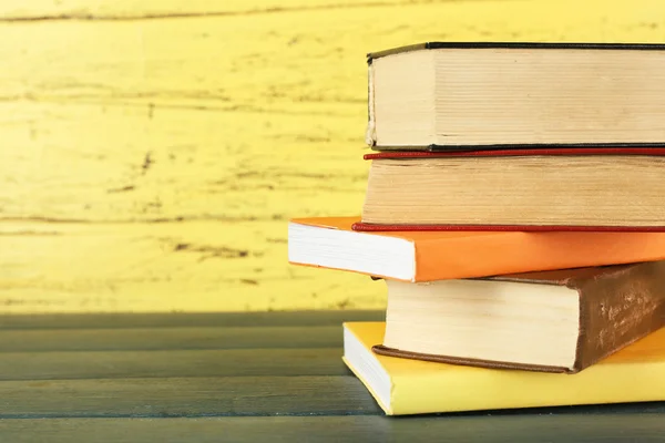 Tumpukan buku di meja kayu dengan latar belakang dinding kayu kuning — Stok Foto