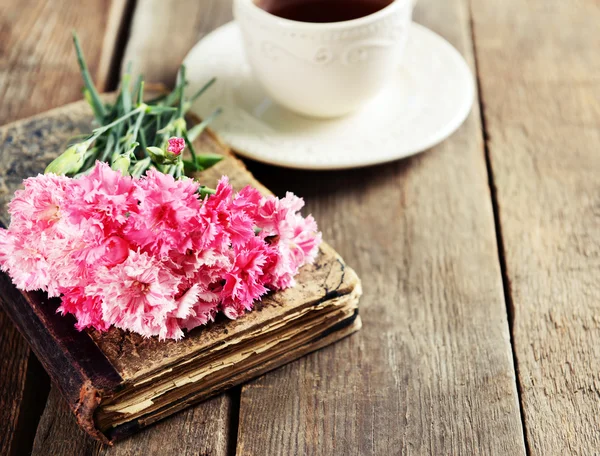 Old book with beautiful flowers and cup of tea on wooden table close up — Stock Photo, Image