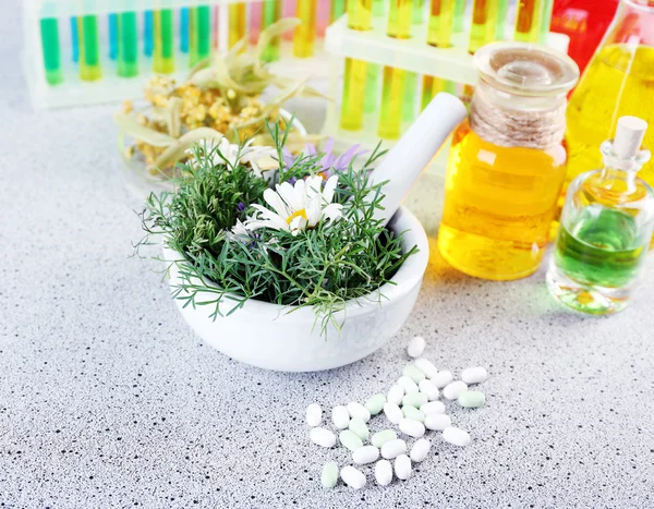 Herbs in mortar, test tubes and pills,  on table, on light background — Stock Photo, Image