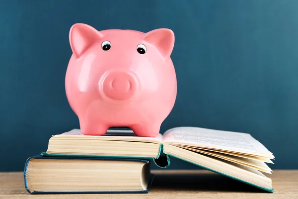 Piggy bank met boeken op schoolbord achtergrond — Stockfoto