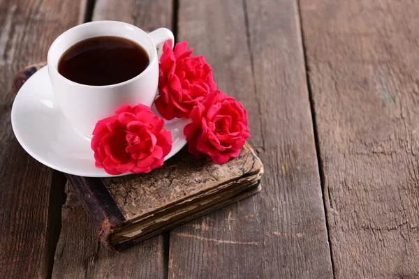 Livro velho com belas rosas e xícara de café na mesa de madeira close-up — Fotografia de Stock