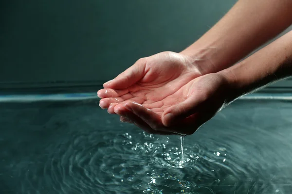 Mains féminines avec éclaboussures d'eau sur fond sombre — Photo