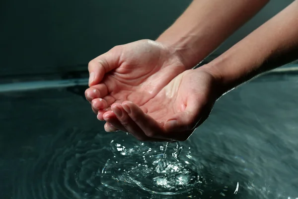 Женские руки с брызгами воды на темном фоне — стоковое фото