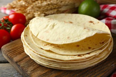 Ev yapımı kepekli un tortilla ve ahşap masa arka plan üzerinde kesme tahtası üzerinde sebze yığını