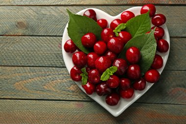 Tatlı kiraz ahşap arka plan üzerinde plaka üzerinde yeşil yaprakları ile