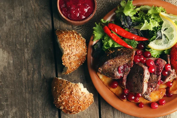 Smaczne mięso pieczone z sosem żurawinowym, sałatki i pieczone warzywa na talerzu, na tle drewniane — Zdjęcie stockowe