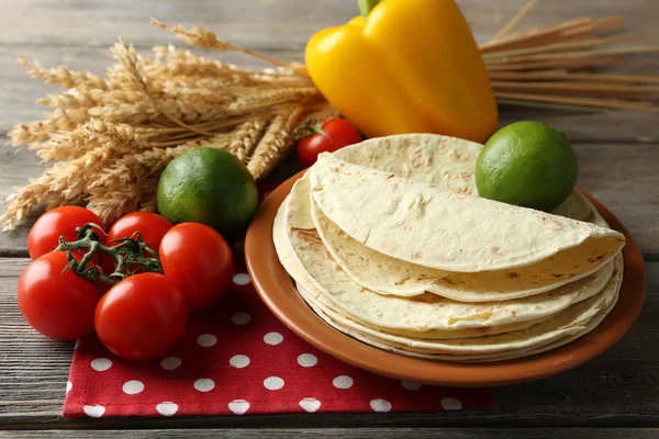 Stack of homemade whole wheat flour tortilla and vegetables on plate, on wooden table background — Stock Photo, Image