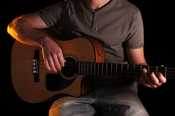 Jeune homme jouant à la guitare acoustique sur fond sombre — Photo