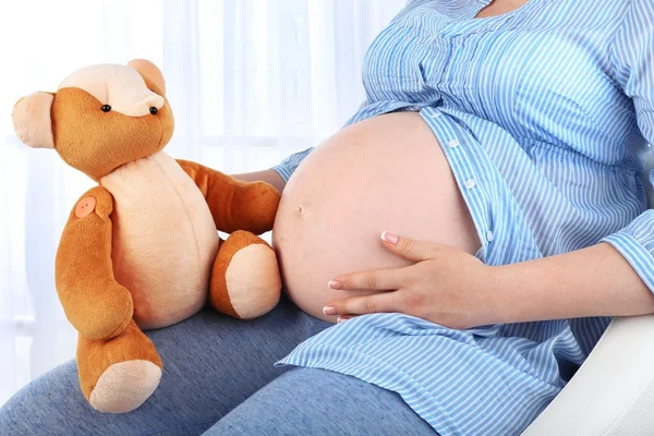 Beautiful young pregnant with baby toy on light background — Stock Photo, Image