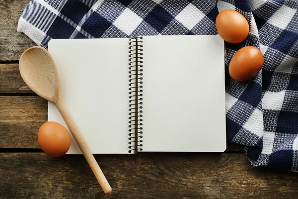 Livro de receitas aberto, ovos e guardanapo em fundo de madeira — Fotografia de Stock