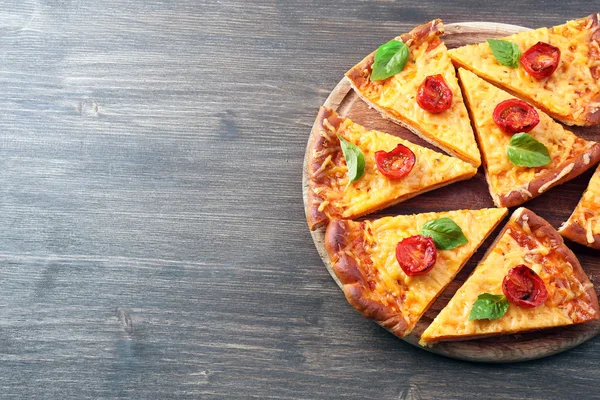 Segmenten van smakelijke kaas pizza met basilicum en cherry tomaten op tafel close-up — Stockfoto