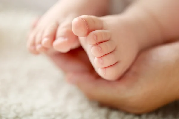 Mãos adultas segurando os pés do bebê, close-up — Fotografia de Stock