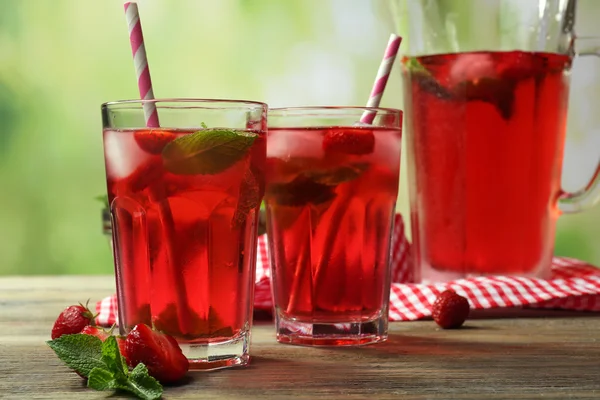 Jarra completa y vasos de jugo de fresa con bayas sobre fondo brillante —  Fotos de Stock