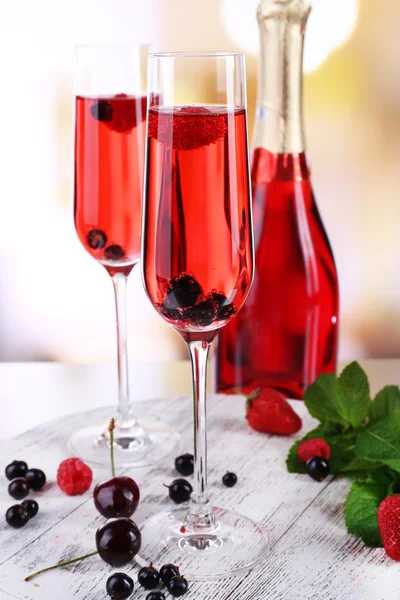 Glass of champagne with berries on light blurred background — Stock Photo, Image