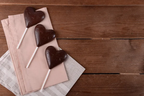Choklad hjärtformade godis på pinnar med servett på trä bakgrund — Stockfoto