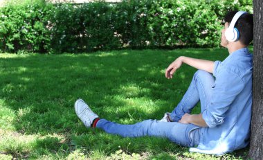 adam parkta ağacın altında oturan kulaklıklar ile