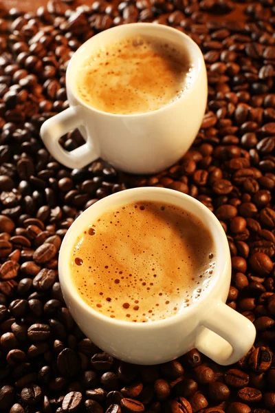 Duas xícaras de café fresco com grãos na mesa, close-up — Fotografia de Stock