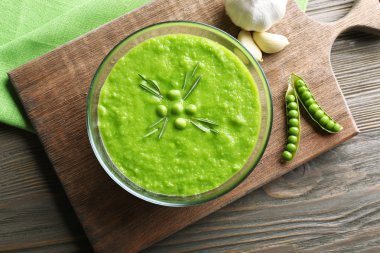 Yeşil bezelye çorbası cam kase üzerinde ahşap kesme tahtası, üstten görünüm