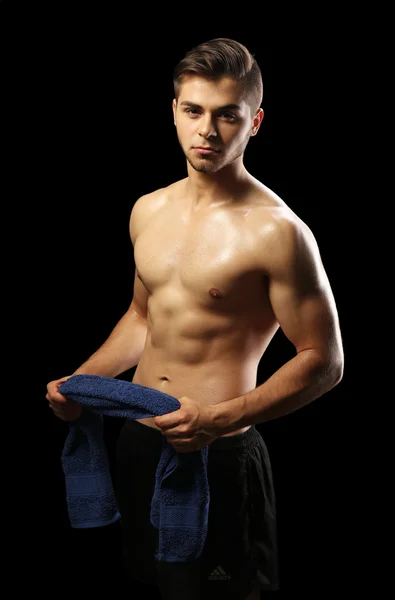 Músculo joven sosteniendo la toalla sobre fondo oscuro — Foto de Stock