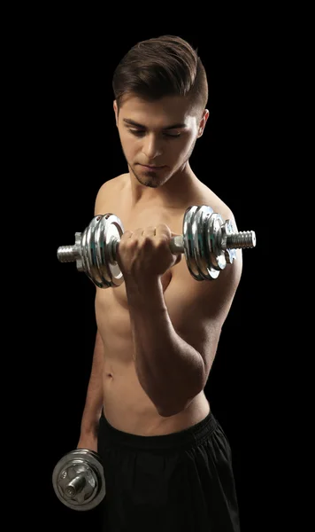 Muscle young man holding dumbbells on dark background — Stock Photo, Image