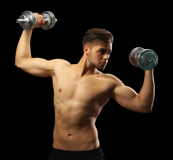 Muskulöser junger Mann mit Hanteln auf dunklem Hintergrund — Stockfoto