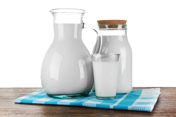 Кувшин, банка и стакан молока на деревянном столе, на белом фоне — стоковое фото