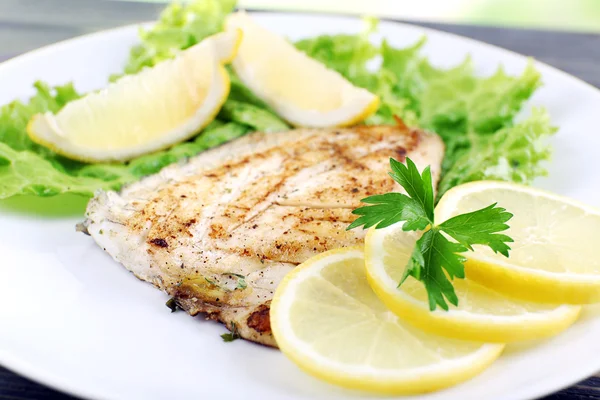Plato de filete de pescado con lechuga y limón en el plato de cerca — Foto de Stock