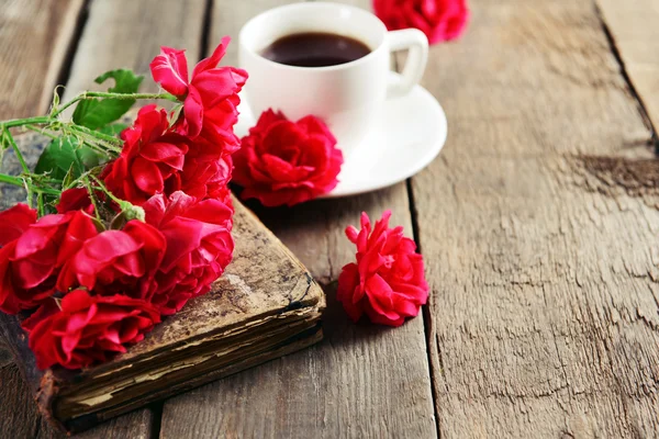 Altes Buch mit schönen Rosen und einer Tasse Kaffee auf einem Holztisch in Großaufnahme — Stockfoto