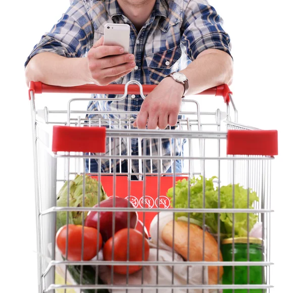 Young man holding mobile phone and shopping cart isolated on white — Stock Photo, Image