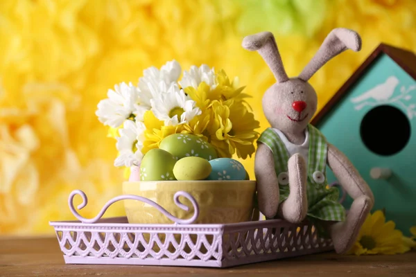 Lapin de Pâques avec des œufs de Pâques peints avec des fleurs sur une table en bois sur fond jaune — Photo