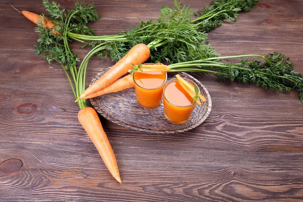 Se acercan los vasos del jugo de zanahoria con hortalizas a la mesa —  Fotos de Stock