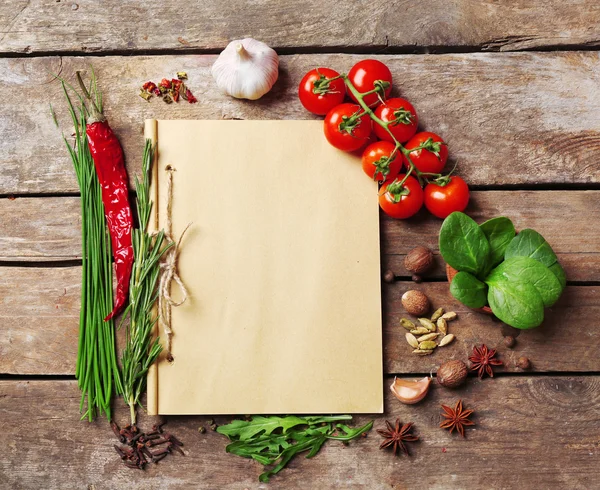 Открыть книгу рецептов со свежими травами, помидорами и специями на деревянном фоне — стоковое фото