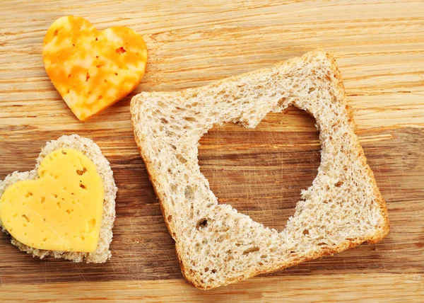 Bread slice with cut in shape of heart and cheese on wooden background — Stock Photo, Image