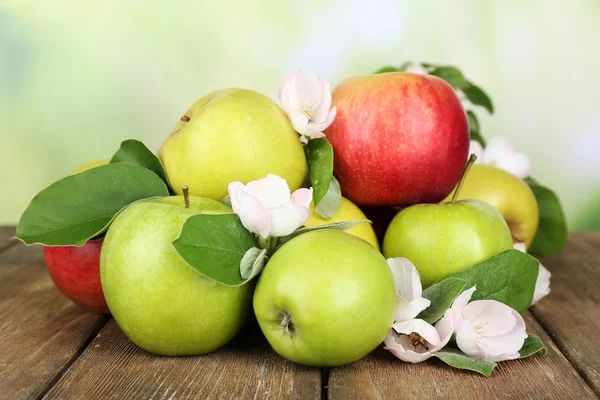 Fresh apples with apple blossom on wooden table, on nature background — Stock Photo, Image