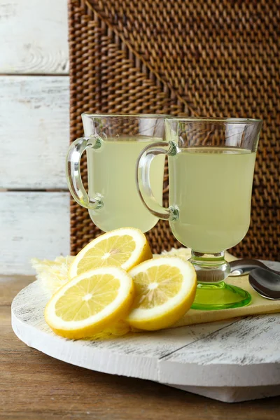 Natura morta con succo di limone e limoni affettati su supporto di legno su fondo stuoia di vimini — Foto Stock