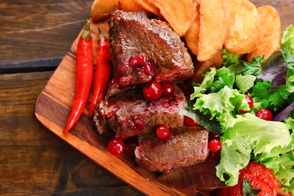 Carne de res con salsa de arándanos, rodajas de patata asadas en la tabla de cortar, sobre fondo de madera — Foto de Stock