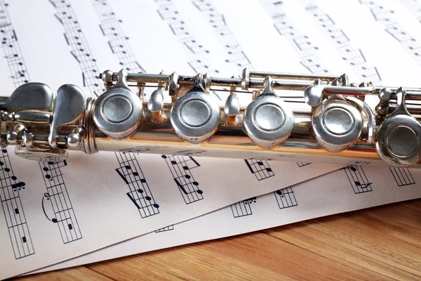 Flauto d'argento con note musicali sul tavolo di legno da vicino — Foto Stock