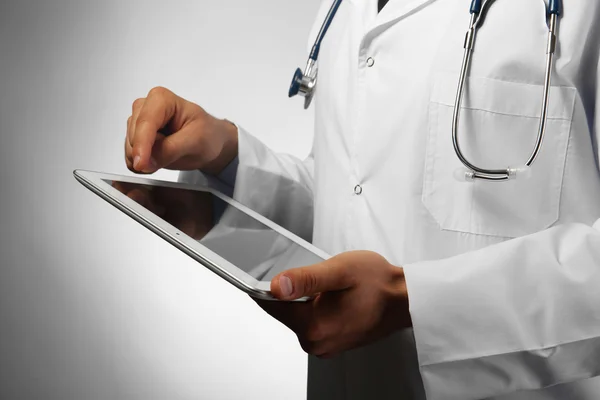 Male doctor with tablet on gray background — Stock Photo, Image