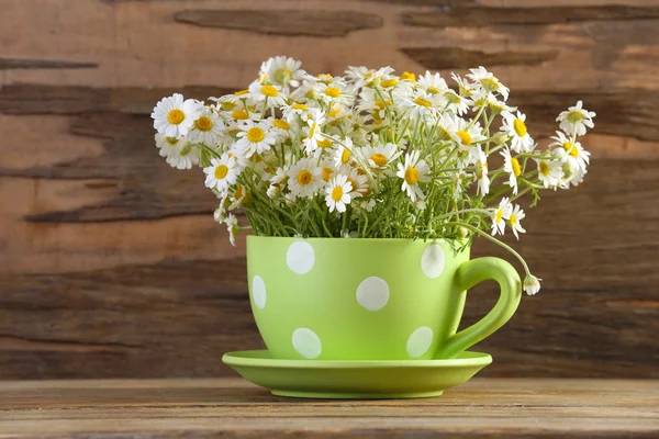 Beautiful bouquet of daisies in cup on wooden background