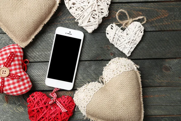 Teléfono inteligente blanco con corazones en escritorio de madera . — Foto de Stock