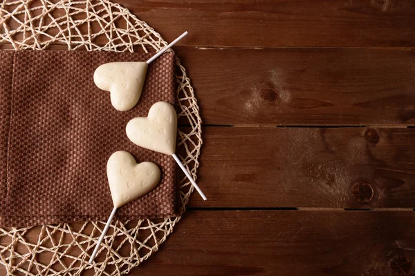 Chocolate caramelos en forma de corazón en palos con servilleta sobre fondo de madera —  Fotos de Stock