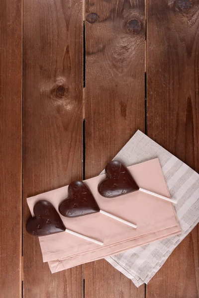 Шоколадные конфеты в форме сердца на палочках с салфеткой на деревянном фоне — стоковое фото