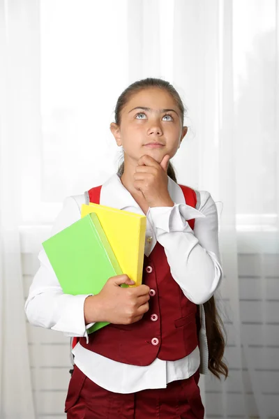 Vacker liten flicka i skoluniform med ryggsäck och böcker — Stockfoto